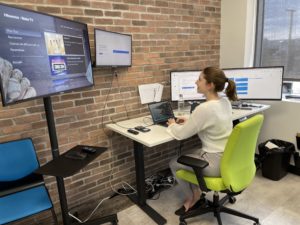 Une travailleuse à son poste dans un bureau fermé en coworking, avec 4 écrans